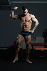 Fototapeta na wymiar Bodybuilder Performing Front Biceps Pose In Gym
