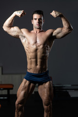 Fototapeta na wymiar Bodybuilder Performing Front Double Biceps Pose In Gym