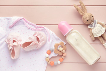 Bottle of milk for baby with toys and clothes on table