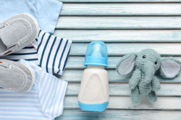 Bottle of milk for baby with toy and clothes on color wooden background