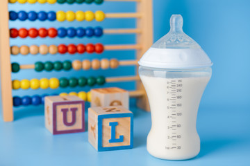 Bottle of milk for baby with toys on color background