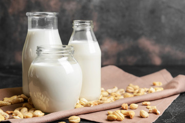 Bottles and jar of cashew milk on dark background