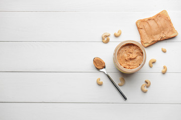 Jar of cashew butter with bread on white wooden background