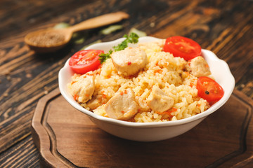 Bowl with tasty rice and chicken on table