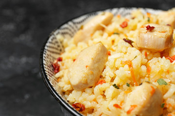 Bowl with tasty rice, chicken and vegetables on dark background, closeup
