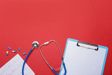 Stethoscope, pills, clipboard and cardiogram on color background