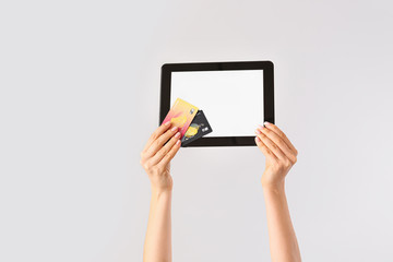 Female hands with credit cards and tablet computer on light background. Concept of online banking