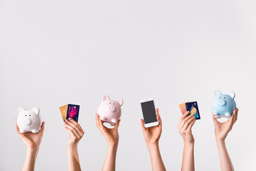 Female hands with credit cards, piggy banks and mobile phone on light background. Concept of online banking - obrazy, fototapety, plakaty