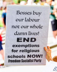 A white political protest banner with black lettering is being held at a religious discrimination...