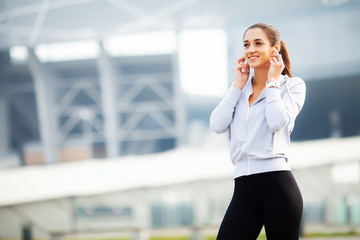 Photo of Joyful Fitness Woman 30s in Sportswear Touching Bluetooth Earpod and Holding Mobile Phone,...