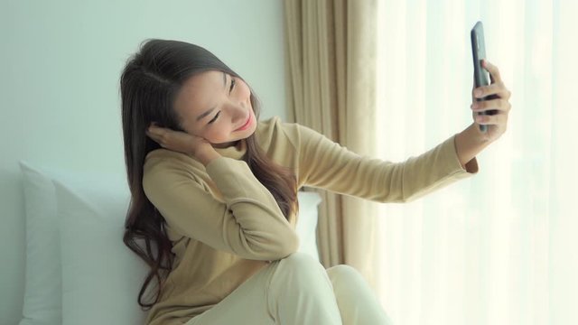 Beautiful Asian girl taking selfie using smartphone at home