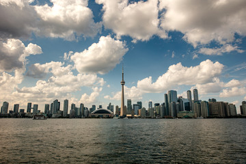 The skyline of Toronto, a view from the lake side - Toronto, Ontario, Canada. Panorama view of the Canadian city of Toronto, with white clouds on a blue sky with the Toronto tower. An urban view