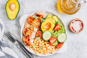 Healthy vegetable buddha bowl lunch with grilled chicken and chickpeas, cucumber, tomato and avocado on light gray background. Top view. Zero waste concept