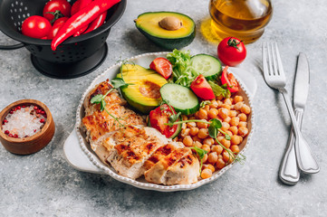 Healthy vegetable buddha bowl lunch with grilled chicken and chickpeas, cucumber, tomato and avocado on light gray background. Zero waste concept. Selective focus