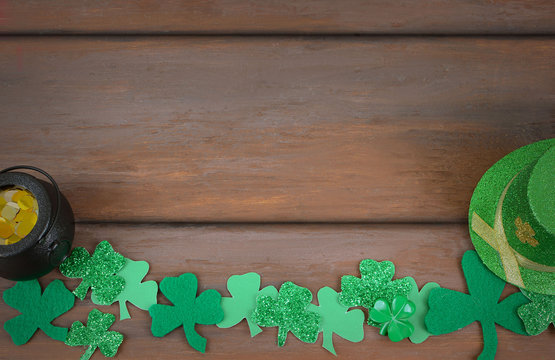 Saint Patrick's Day image of glittered and felt green sharmocks form a border on a rustic wooden background. A pot of Gold and a Leprchaun hat added..Copy space.