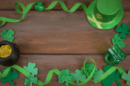 Saint Patrick's Day image of glittered green and felt sharmocks woth ribbon form a border on a rustic wooden background. Leprechaun hat and pot of gold included.