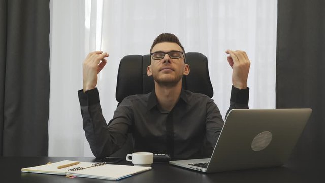 Businessman sitting at his office desk in dzen position. Man broker meditating at workplace. Male trader relaxing after hard working day in office. Man sitting in modern office. Business concept