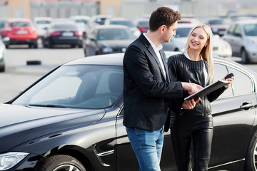 Happy young couple chooses and buying a new car for the family