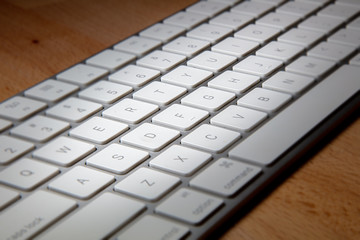 Close up of a white aluminum keyboard on a wooden desk.  Macro photography of a wireless computer keyboard. White keys on a silver frame. Detailed shot of a modern computer keyboard on wood 
