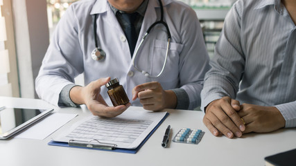 Fototapeta premium Confident doctor man holding a pill bottle and writing while talking with senior patient and reviewing his medication at office room.