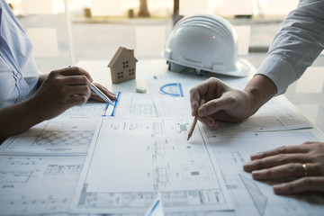 Two architect working at construction site and compass drawing pointing on blueprint with partnership.