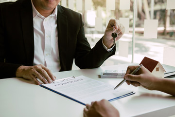 Hand of real estate agent passes the key to new homeowners in office with buyer house concept.