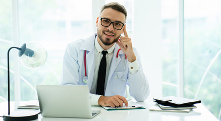 Caucasian doctor, with a mustache, sitting, working in a hospital room or clinic with laptop to...
