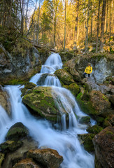 Fototapeta na wymiar hiker in yellow rain jacket standing in front of waterfall on a moody day in Austria