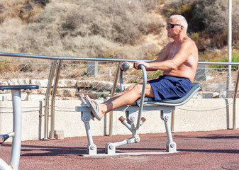 Fototapeta na wymiar Adult man doing exercises on a sports simulator on the sports ground
