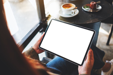 Mockup image of a woman holding black tablet pc with blank white screen in cafe