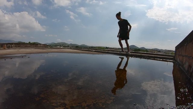 slow motion video of a young freerunner jumping a sideflip creating a mirror effect in a puddle on a roof  of a abandoned building