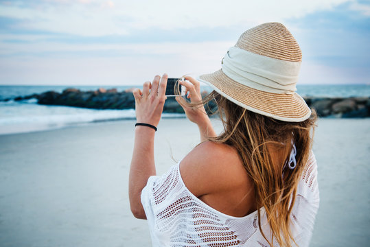 young woman on the beach taking a picture with her phone
