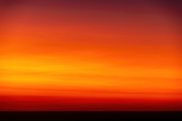 View of bright orange and red sunset sky over Tasman sea horizon from Piha beach
