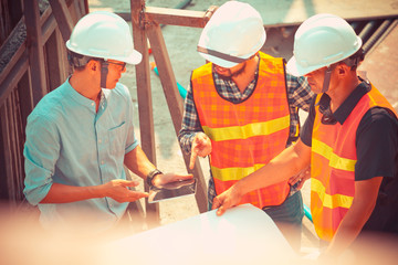 The engineers clear shop drawing plan with mobile phone and blueprints for management business plan., consultation to discuss and solve the problem together at construction site.