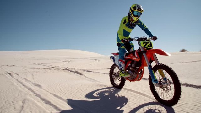 Motocross rider performing a wheelie and stopping his bike in desert. Stunt biker displaying his riding skills on sand dunes.