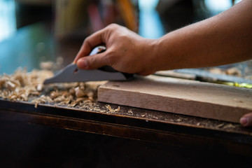 Wood shavings carpenter working with a metal spokeshave and a blurry background. Light beige colored poplar wood with slight curves in it. Vintage woodworking, handwork, handmade
