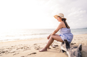 Young asian woman sitting with hat on the beach with sunset sky background, summer concept and travel concept.