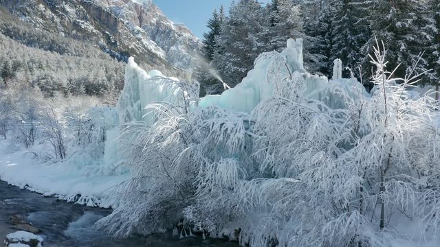 Winter view in northern Italy, Dolomites. Snowcovered trees and fields. Rushing icy cold water in the river. Ice sculptures. Mountains towering in the background.