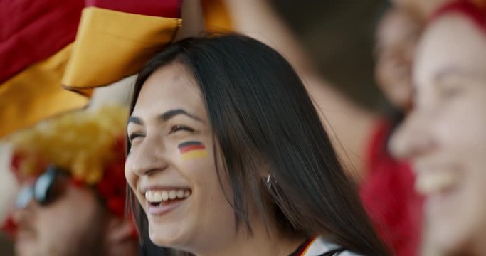German soccer supporters cheering during a live match at stadium. Woman with friends enjoying in fan zone.