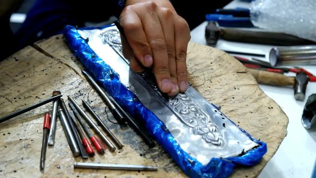 Hands of professional artisan craftsman using tool carving Thai pattern on metal plate to make local traditional handmade handcraft carved artwork