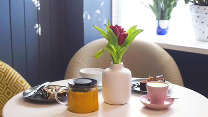 Breakfast with coffee, tea and pastries at a cozy table of a modern cafe by the window.