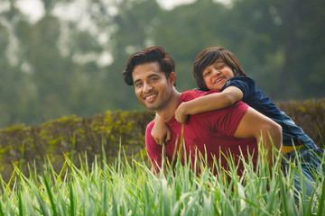 Happy young boy piggy riding on the back of his father outdoors with fresh grass in the foreground.