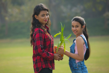Fototapeta premium Smiling young girl giving a plant in a flower pot to her mother outdoors.
