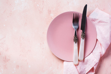 Pink plate, cutlery and napkin on stone table top view. Table setting.