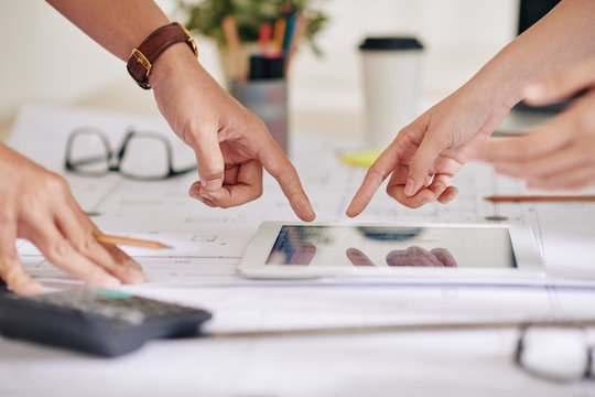 Hands of arhitect and construction engineer pointing at building plan on screen of tablet computer