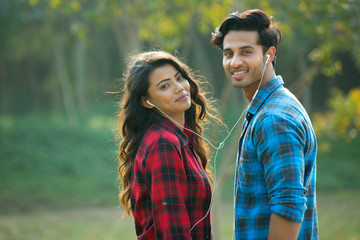 Young couple standing in a garden sharing an earphone listening to music.