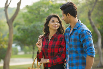 Smiling young couple walking outdoors with the man putting his arm around the woman looking at each other.