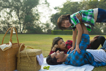 Happy man and woman on a picnic lying down in garden beside picnic baskets and the man is playing...