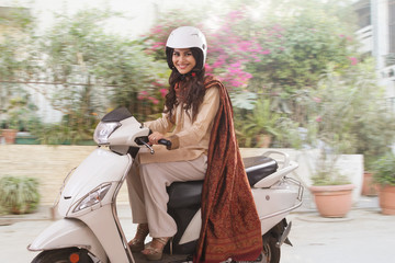 Smiling young woman in traditional dress riding a scooter wearing a helmet.