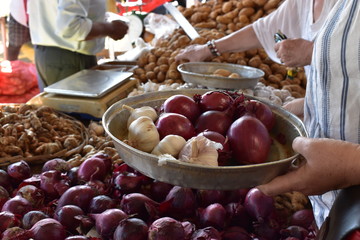 Detail of unknown buyer selecting red onions, garlic et other condiments.